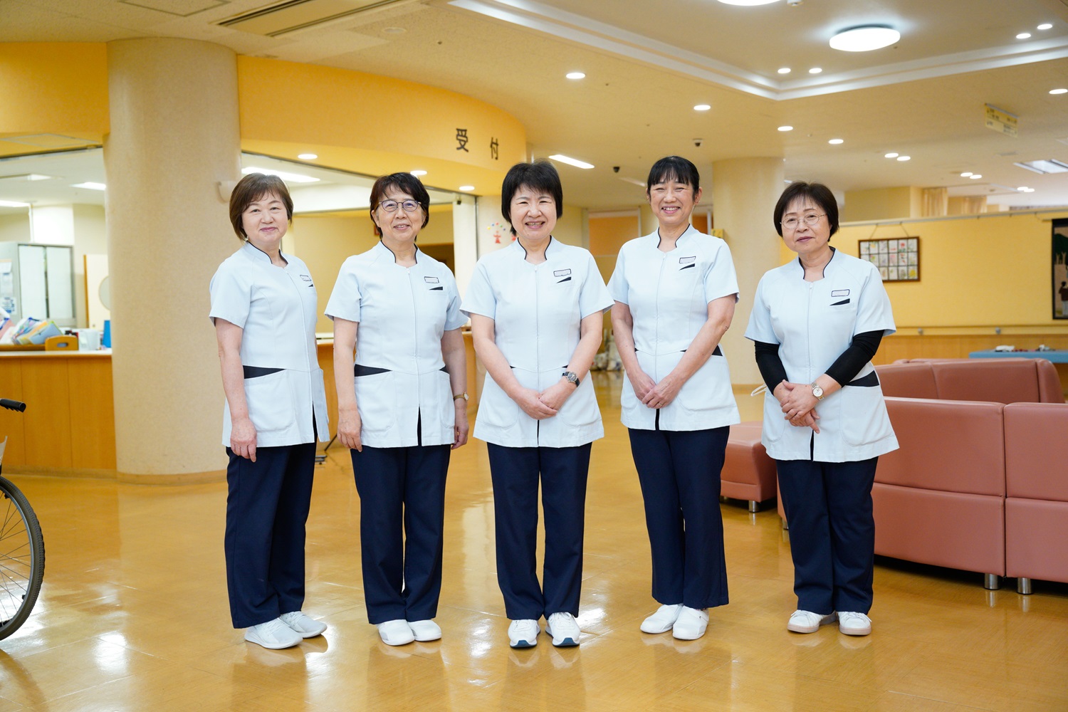 介護施設のスタッフ5名が制服姿でロビーに並んで立つ