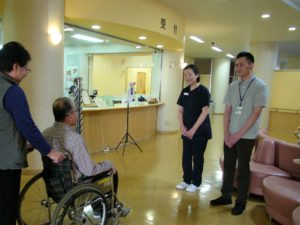 ロビーで車椅子利用者とスタッフが交流している様子。受付カウンターが見える。